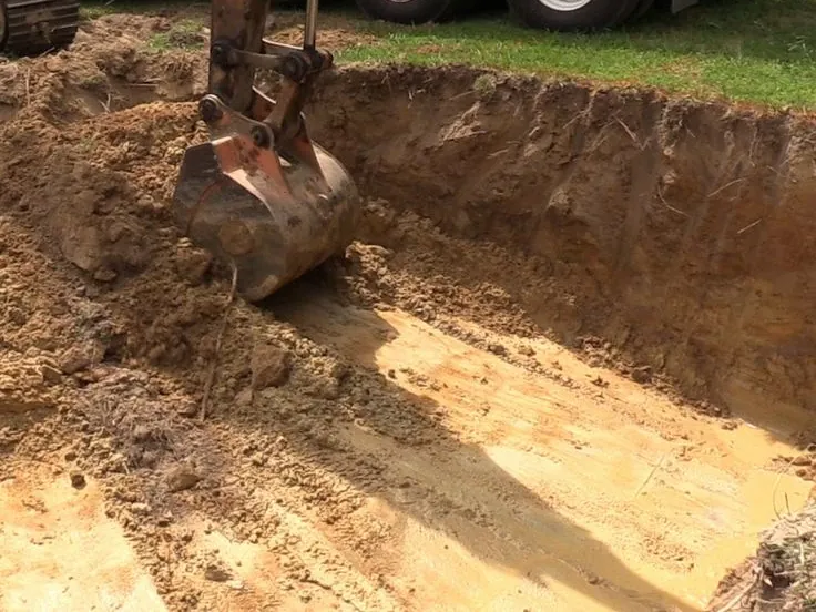 Excavator bucket cutting the wall of an in-ground pool hole